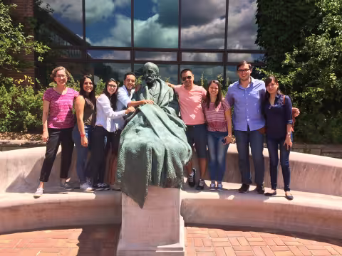 A small group of students stand next to a statue outside a glass building on a sunny day.