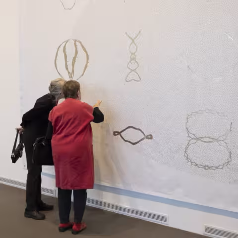 Visitors at the museum looking close up to artwork on the wall.