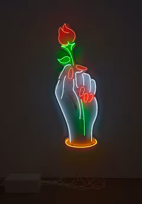 Neon sculpture of a white hand, with red nails, holding a red rose.  