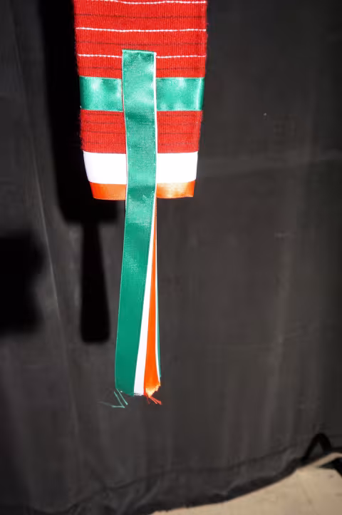 A man's red fabric belt with green, white and red silk ribbons.