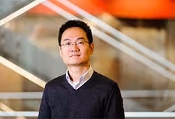 Ming Yuan in glasses, a dark v-neck sweater with a collared shirt