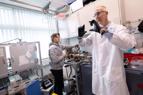 A man in a white lab coat gestures making a rectangle with his fingers clad in black gloves.