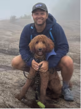 A portrait of Phil with his brown dog in front of him.
