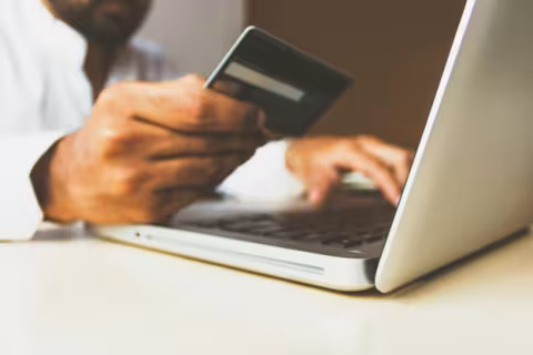 A person holds a credit card in their right hand while typing on a laptop with their left