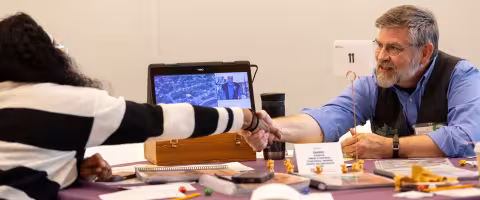A researcher and a student seated at a table shake hands during a RISE pitch session.
