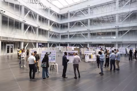 People stand around research posters inside a large spacious building