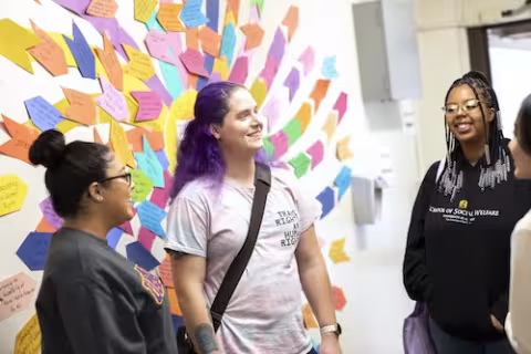 Students engaged in discussion in front of white board with many colorful post-it notes.