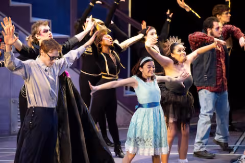 Student actors in costume and makeup dance on stage during dress rehearsals