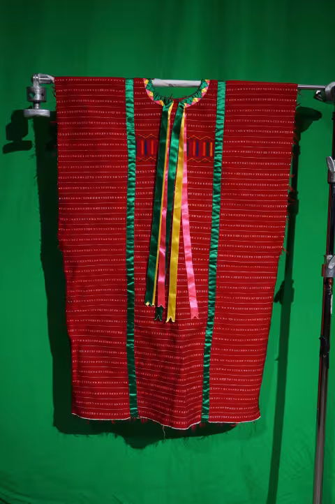 A woman's red fabric huipil with green, yellow and pink silk ribbons.