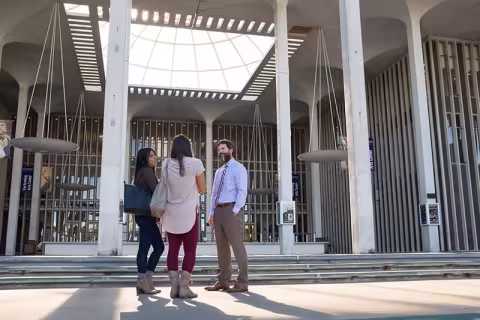 two students talking with a professor on campus