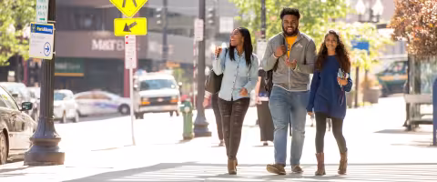 Three UAlbany students smile and laugh as they walk through downtown Albany on a sunny day.