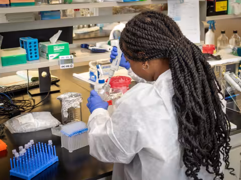 Ariana Nobles in the Mantis Lab at Wadsworth. She wears a white protective coat and blue latex gloves.