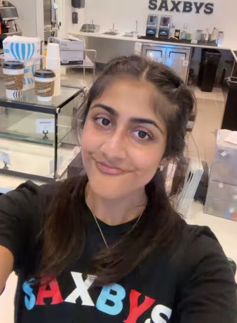 A young woman with dark hair wears a shirt that says SAXBYS while working inside the new Saxbys location in UAlbany's Massry School of Business