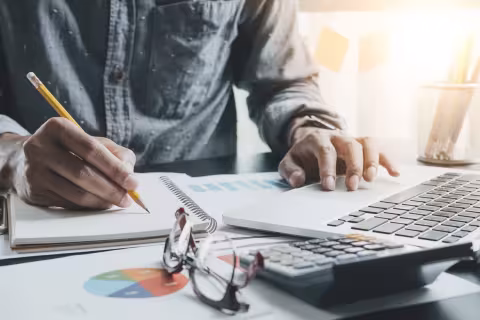 An accountant making notes and working on a laptop