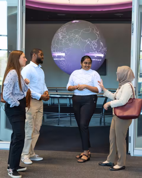 Four students having a discussion in front of a globe in UAlbany's ETEC building.