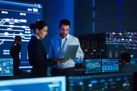Two professionals working on a laptop in a computer data center.