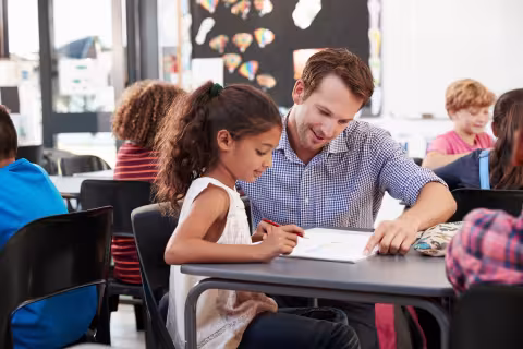 A teacher working with a young student in classroom.