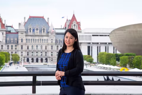 A student standing on Albany's Empire State Plaza with the Capitol building in the background.