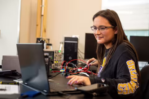 A student working on a laptop and equipment in a UAlbany engineering lab.