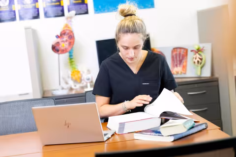 A nursing student studying with textbooks and a laptop.