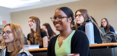 Multiple students laugh and smile while seated inside a classroom with tiered rows of seating.