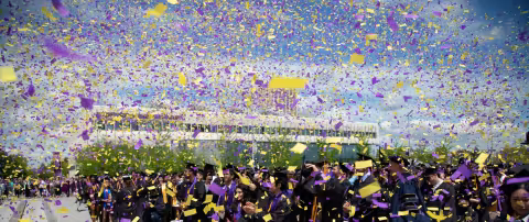 Purple and yellow confetti falls upon celebrating UAlbany graduates in Commencement regalia.