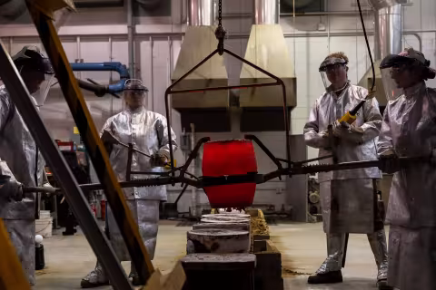 Four people carefully operate a crucible during a bronze metal pour at the Boor sculpture studio at UAlbany.