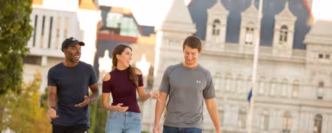 Three students smile and laugh as they walk along the Empire State Plaza near the Capitol.
