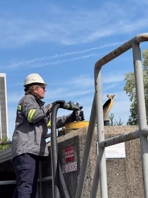 a man in a grey jacket and a white hardhat puts fuel into a tank