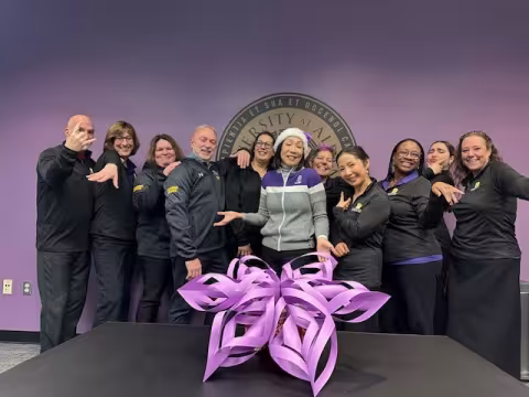 Eleven staff members from the Provost's Office pose for a lighthearted photo with a large purple paper snowflake.