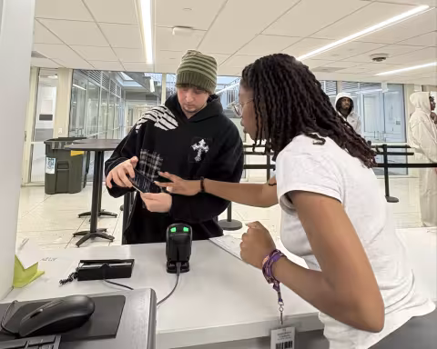 A student points to another student's phone from behind a mailroom counter