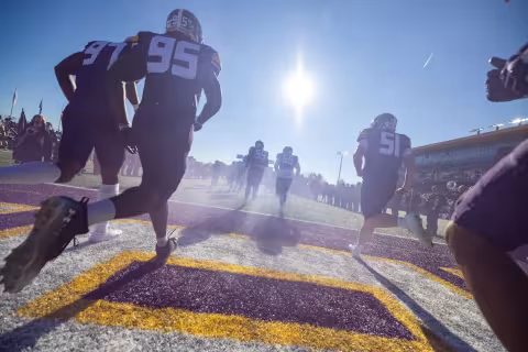 A group of UAlbany football players running onto the field.