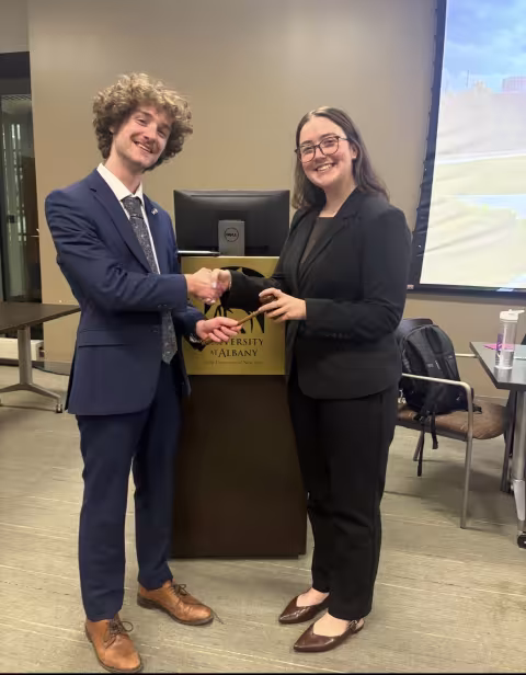 Junior Troy Serao shakes hands with a fellow classmate in front of a UAlbany podium.