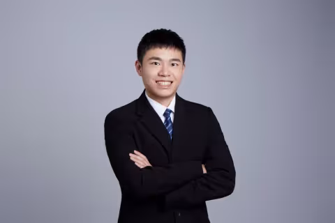 A profile photo of Zong-Xian (Sam) Huang wearing a dark suit and tie against a gray background
