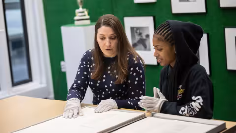 A faculty member and a student wearing white gloves handle a manuscript in the University Archives.