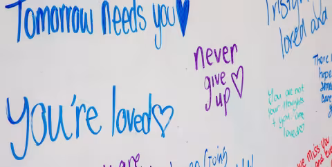 Encouraging messages are written on a whiteboard during UAlbany's annual Out of the Darkness Walk. Messages read "tomorrow needs you," "you're loved," "never give up" and "you are not your thoughts and you are loved."