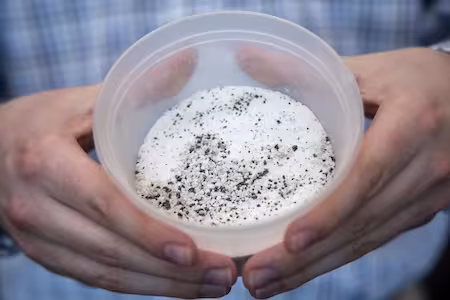Hands hold a container of lunar regolith simulant