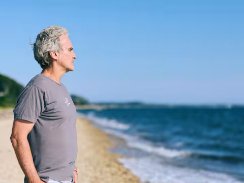 A man standing on a beach with the waves on his right and a dune in the background.