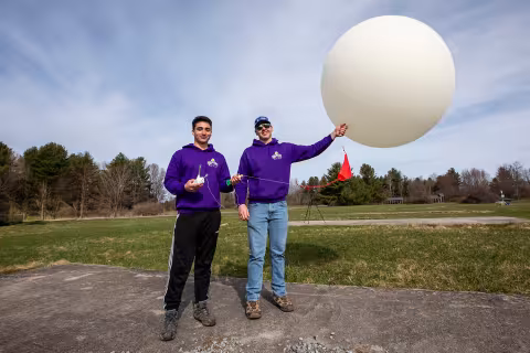 Two students in purple UAlbany sweatshirts prepare to launch a weather balloon.