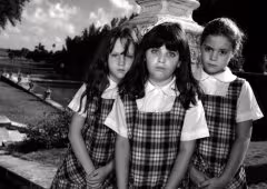Three young people look at the viewer, wearing matching plaid dresses.