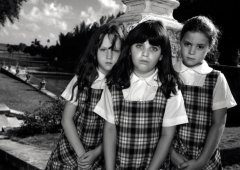 Three young people look at the viewer, wearing matching plaid dresses.