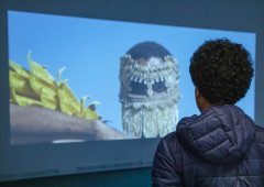 A person stands in front of a projection, watching it.