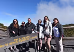 A small group of students and a faculty member stand beside a sign in Spanish. They are outdoors and a clear blue sky is behind them.