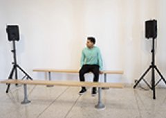 A person sits in the exhibition space with speakers near them.