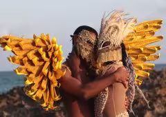 Two people embrace, wearing intricate masks.