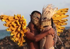Two people embrace, wearing intricate masks.