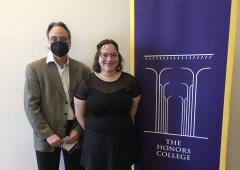 John Justino and Evelyne Nehama stand next to a purple pull up banner than says "The Honors College". 