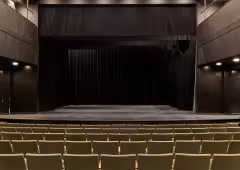partial shot of small proscenium stage with drab green seats