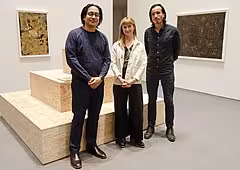 Three people pose, smiling, in front of an art installation.