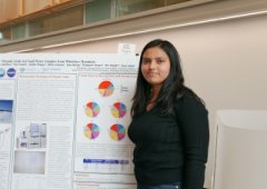 A woman with long dark hair wearing a long-sleeved black shirt stands in front of a presentation poster.